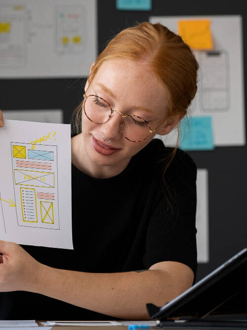 A UX designer explaining a wireframe sketch during a usability testing session, with design drafts and sticky notes in the background.